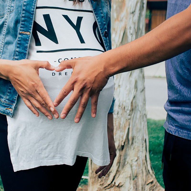 Two hands making the shape of a heart over a pregnant belly